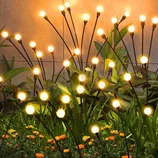 Solar-powered garden stake lights with warm white LED bulbs, resembling glowing flowers, are surrounded by various plants and colorful marigolds.