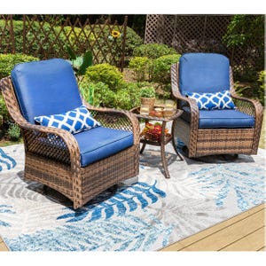 Outdoor wicker furniture set with two blue cushioned chairs and a small round table, located on a patterned outdoor rug in a garden setting.