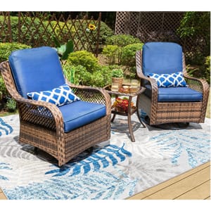 Outdoor wicker furniture set with two blue cushioned chairs and a small round table, located on a patterned outdoor rug in a garden setting.