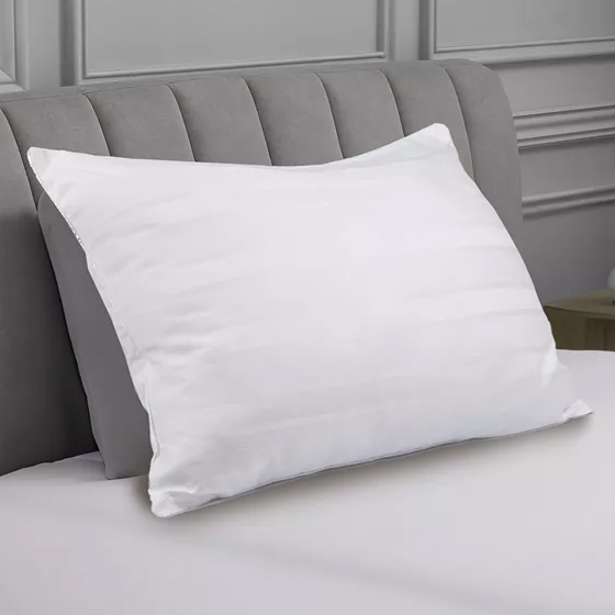 White cotton pillow with a striped pattern, resting on a light gray upholstered headboard.