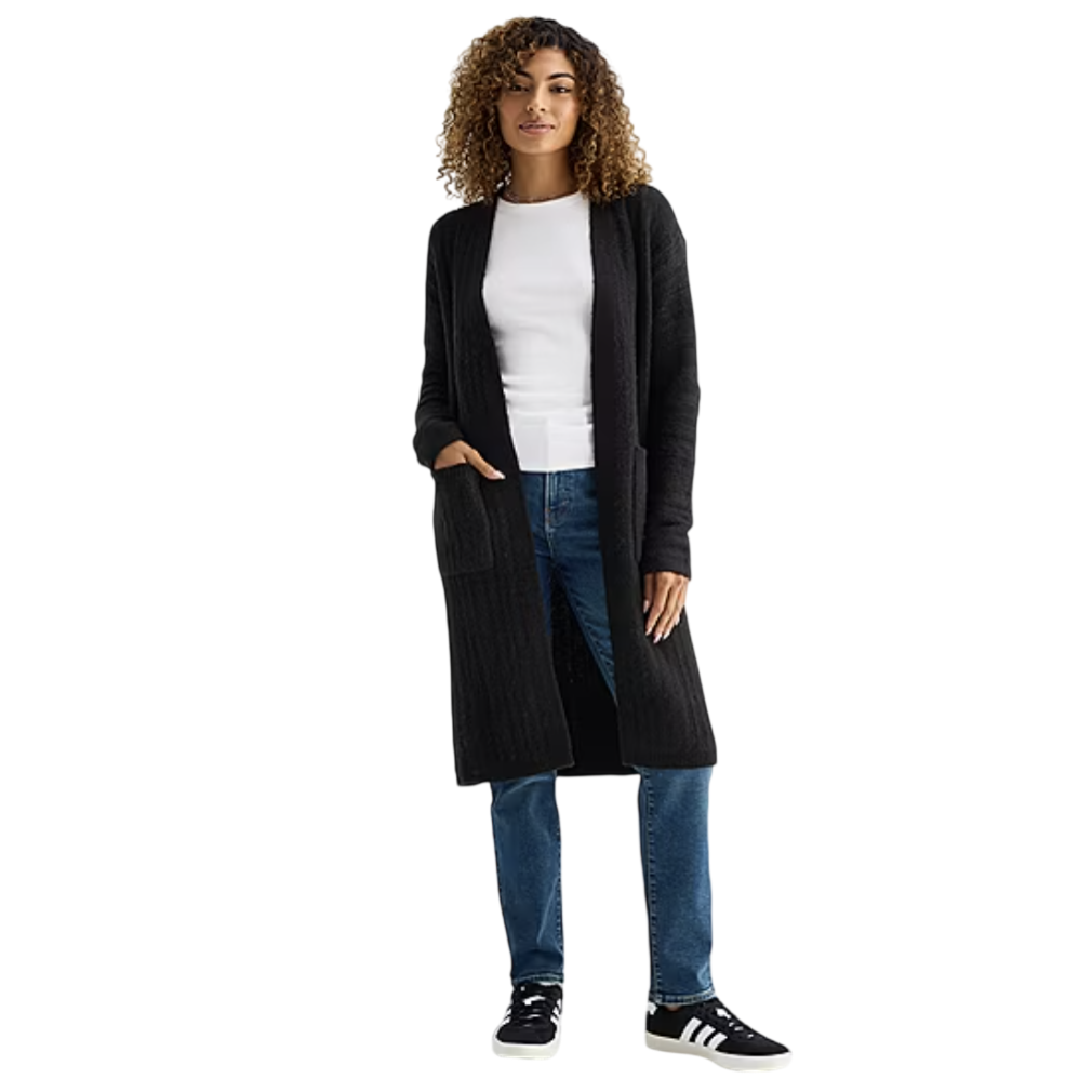 A woman is wearing a black long cardigan, a white top, blue jeans, and black sneakers with white stripes.