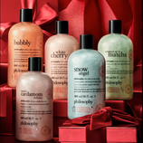 Five Philosophy shower gels: Bubbly, White Cherry, Snow Angel, Wrapped Up in Matcha, and Special Cardamom Delivery, each in 480 ml bottles, set against a backdrop of red gift boxes and bows.