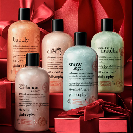 Five Philosophy shower gels: Bubbly, White Cherry, Snow Angel, Wrapped Up in Matcha, and Special Cardamom Delivery, each in 480 ml bottles, set against a backdrop of red gift boxes and bows.