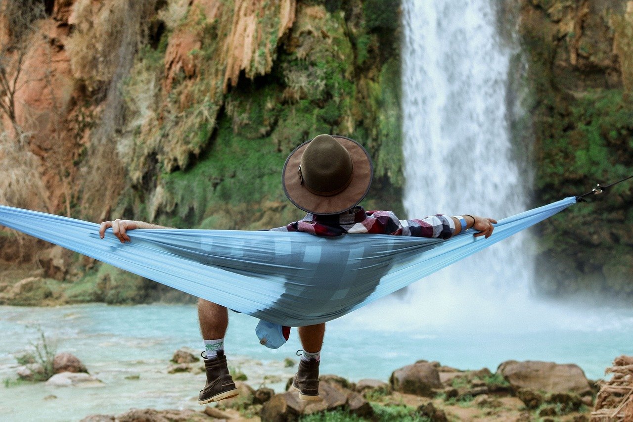 A person relaxes in a hammock in front of a waterfall