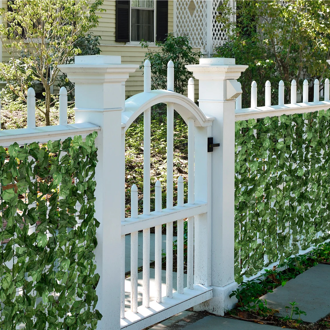 A white picket fence gate with a curved arch top, attached to a traditional picket fence with ivy.