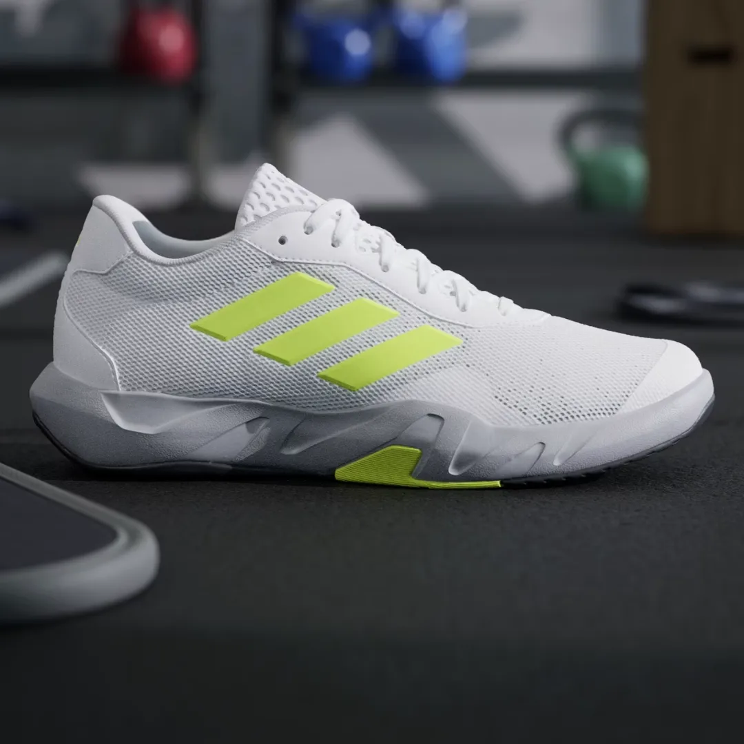 A white athletic shoe with neon green accents and laces, displayed in a gym setting.