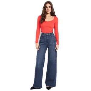 A woman is wearing a long-sleeve, red top and high-waisted, wide-leg jeans paired with black shoes.