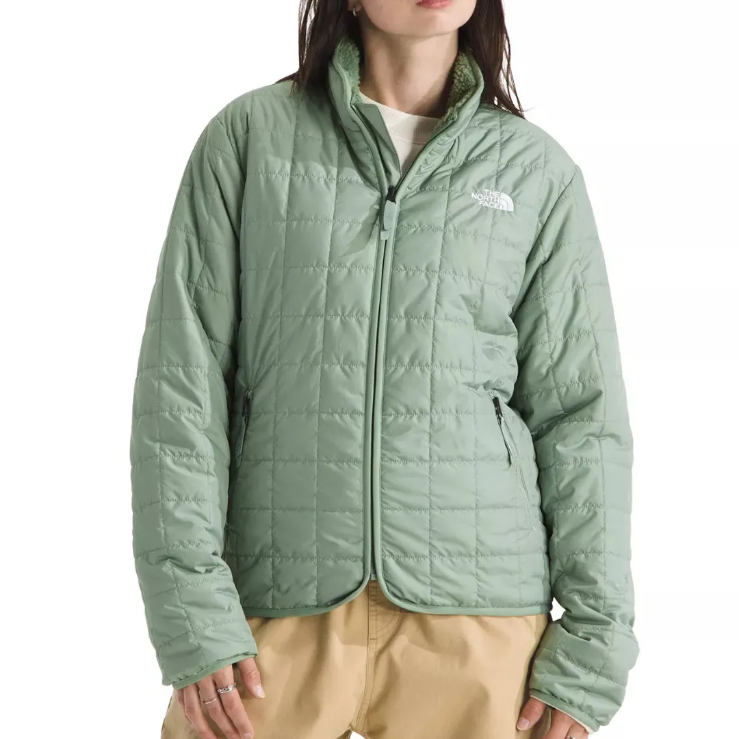 A light green quilted jacket with a full zip, two side pockets, and a discreet logo on the chest, worn by a person paired with beige pants.