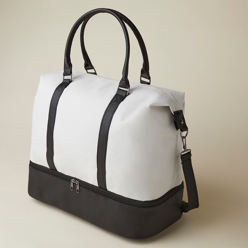 A two-tone weekender bag featuring a white upper portion and a dark base, with black straps and a detachable shoulder strap; the bag has a zippered closure on top.
