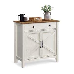 A rustic white cabinet with a wooden top, featuring a drawer and two crossbuck-patterned doors. Decorated with a small pitcher, plant, and woven basket.