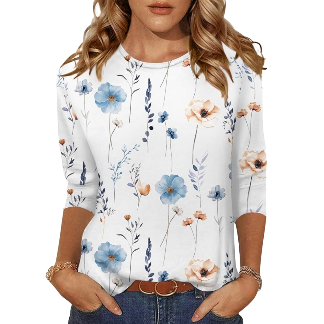 A woman wears a white blouse with a floral print featuring blue and peach flowers, paired with blue jeans and a brown belt.