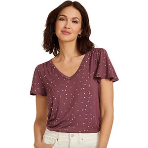 A woman wearing a mauve short-sleeve V-neck top with small white polka dots, paired with light-colored pants.