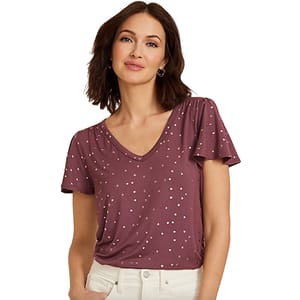 A woman wearing a mauve short-sleeve V-neck top with small white polka dots, paired with light-colored pants.