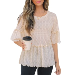 A woman holds a coffee cup while wearing a light, textured blouse with a frilled hem and sleeves, paired with dark pants.