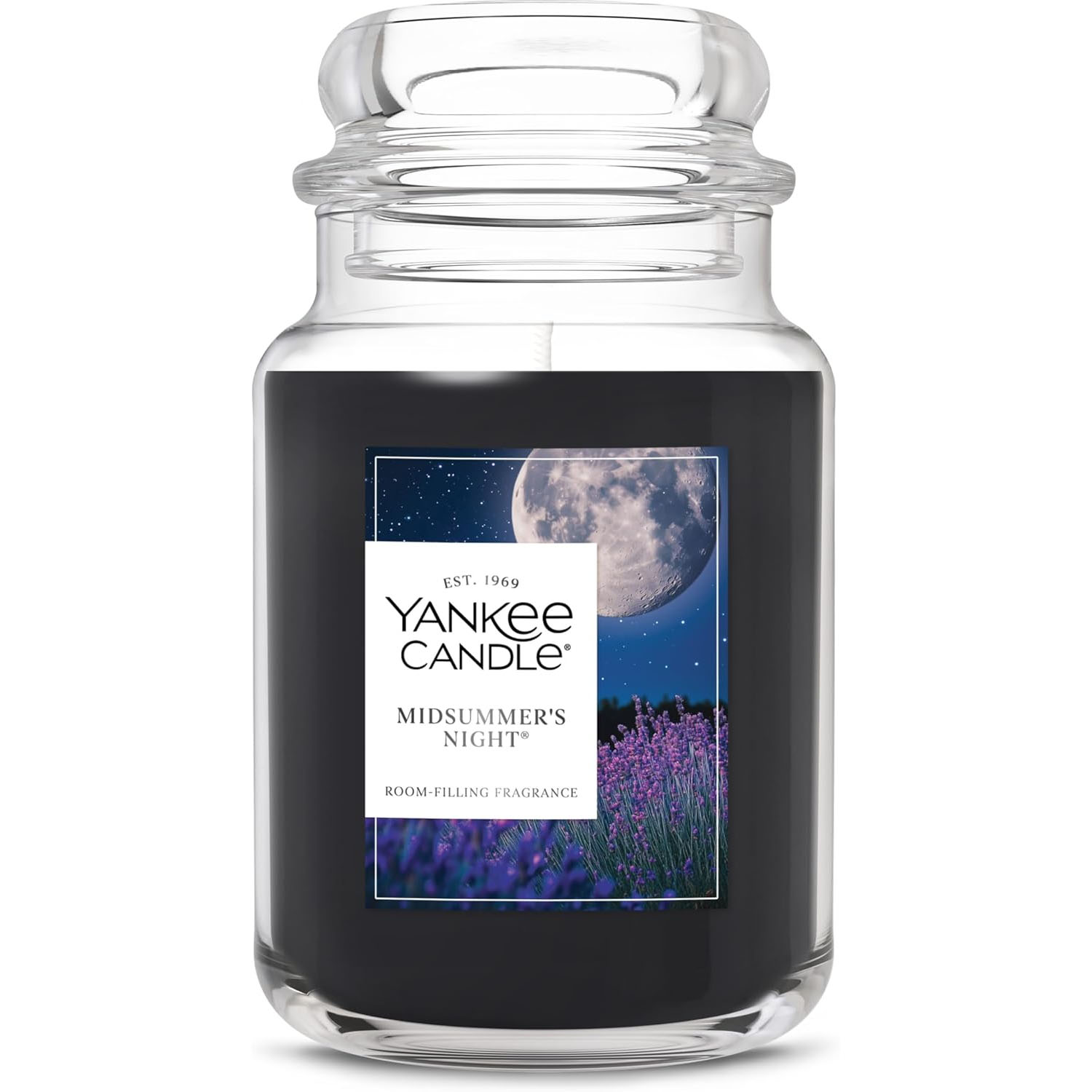 Yankee Candle \“Midsummer's Night\“ features a dark-colored wax in a classic clear jar. Fragrance: room-filling, with a label depicting a starry night and full moon above lavender fields.