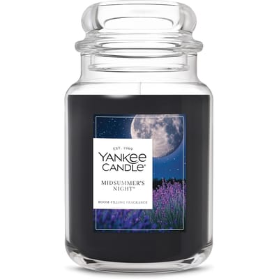 Yankee Candle \“Midsummer's Night\“ features a dark-colored wax in a classic clear jar. Fragrance: room-filling, with a label depicting a starry night and full moon above lavender fields.