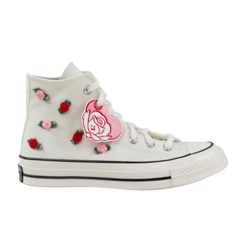 A white high-top sneaker featuring embroidered red and pink roses with green leaves, and a pink heart-shaped rose illustration tag attached to the laces.