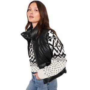 A black faux-leather puffer vest with a high collar, featuring snap button closures, worn over a black and white geometric-patterned sweater.