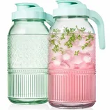 Two glass pitchers with textured designs and mint green lids, one filled with pink liquid, ice, and herbs.