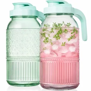 Two glass pitchers with textured designs and mint green lids, one filled with pink liquid, ice, and herbs.