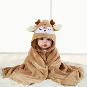 A baby is wrapped in a brown hooded blanket designed to look like a deer, complete with antlers and ears, sitting on a soft, white rug.