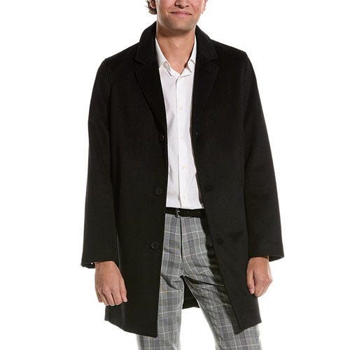 A man wearing a black overcoat over a white dress shirt and plaid trousers.