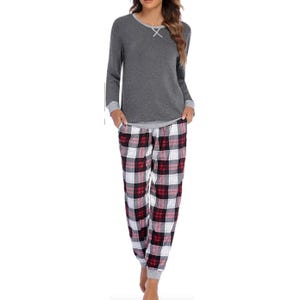A woman wearing a gray long-sleeved top with a crisscross neckline detail and plaid pajama pants in shades of red, white, and black.