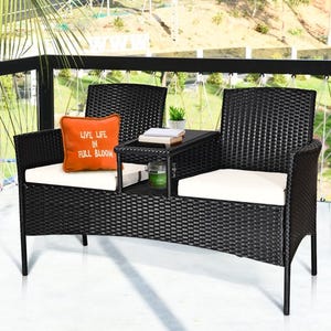 Black outdoor furniture set with two chairs, a loveseat, and a central table, featuring white cushions and an orange decorative pillow.