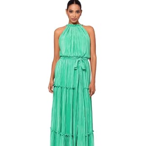 A woman is wearing a sleeveless, halter-neck, pleated gown in a vibrant green color with a tie waist detail.