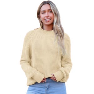 A woman is wearing a cream-colored, long-sleeve knit sweater paired with blue jeans.