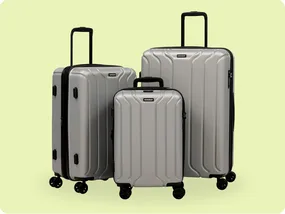 Three silver hard-shell suitcases with four wheels each, varying in size, positioned against a light green background.