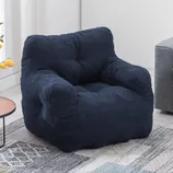 A navy blue armchair with a soft, plush texture and a cozy, tufted design, suitable for living room settings. The chair is placed on a patterned rug next to a wooden side table with lemons.