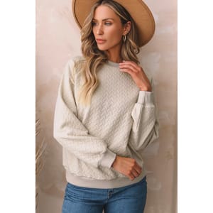 A woman wearing a cream cable knit sweater and a tan wide-brimmed hat paired with blue jeans.