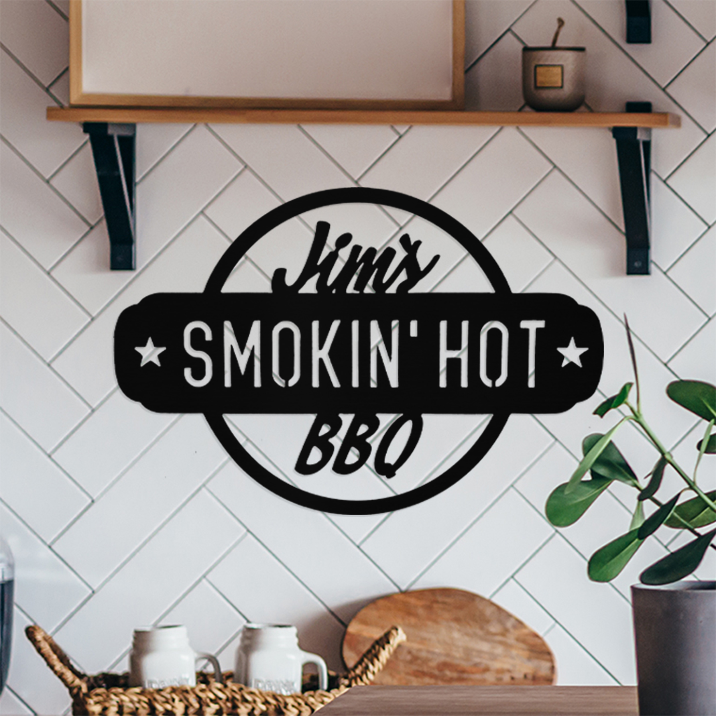 A personalized wall sign with the text \“Jim's Smokin' Hot BBQ\“ is displayed on a kitchen wall featuring a herringbone tile pattern. It has a circular design with stars flanking the text.