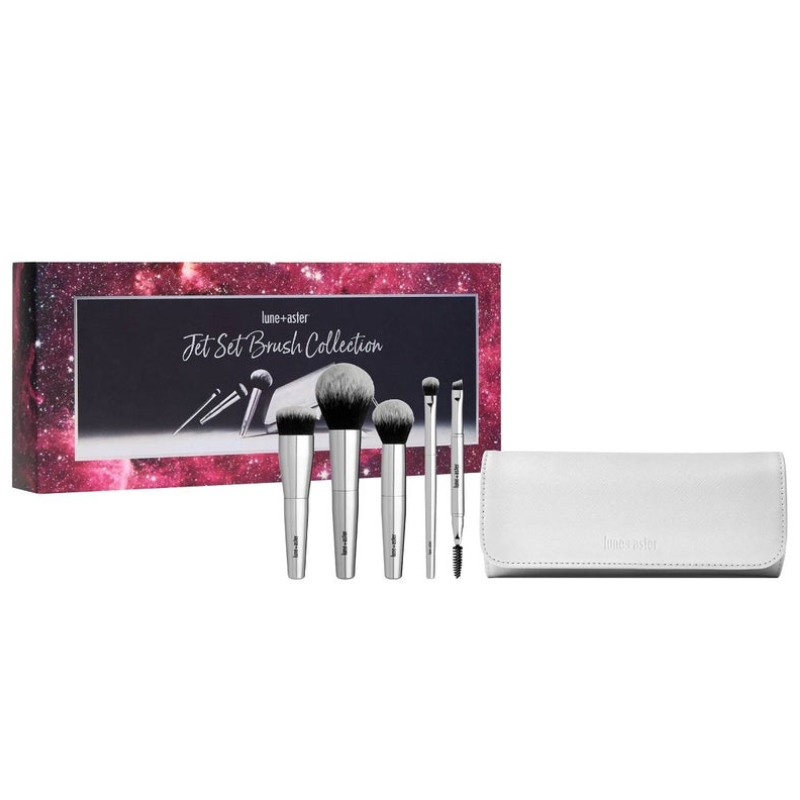 5-piece Lune & Aster Jet Set Brush Collection includes a face brush, powder brush, shadow brush, blending brush, and spoolie, paired with a white carrying case. The set is packaged in a box with a pink and purple cosmic design.