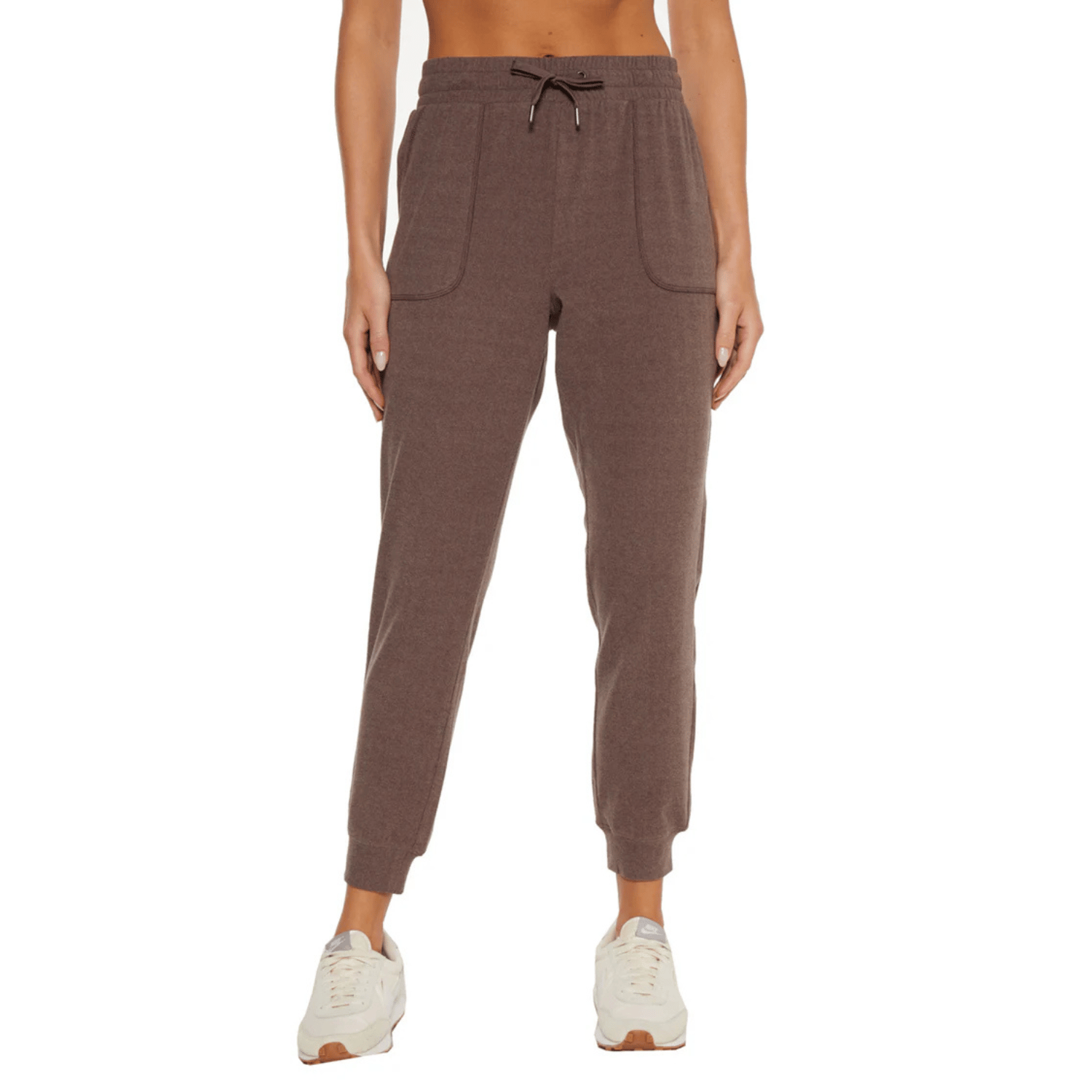 Brown joggers with an elastic waistband, drawstring, and two front pockets. They have a cuffed ankle design and are worn with white sneakers.
