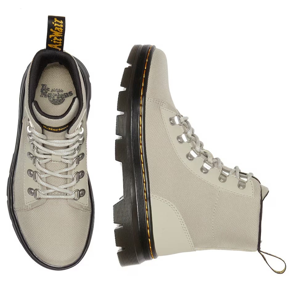 Canvas high-top booties in light gray with lace-up fronts, black and yellow pull loops, and thick, grooved soles with contrasting yellow stitching.