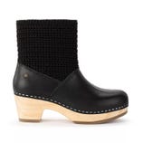Black ankle boot with a wooden sole, featuring a textured, knitted upper section and a small decorative emblem.