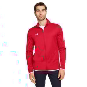 A man is wearing a red Under Armour track jacket with a white logo on the chest, featuring a full zip front and white accents on the cuffs and shoulders.