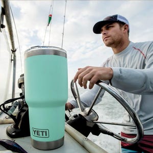 A man steers a boat holding a YETI branded tumbler.