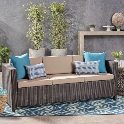 A brown patio sofa with beige cushions and blue pillows.