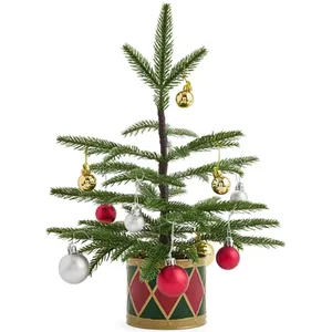 Small Christmas tree with red, gold, and silver ornaments in a decorative pot featuring a red and green diamond pattern.