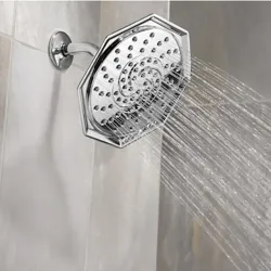 A chrome octagonal showerhead sprays water in multiple streams against a tiled wall.
