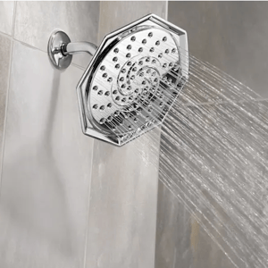 A chrome octagonal showerhead sprays water in multiple streams against a tiled wall.