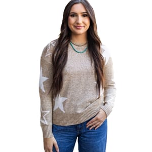A woman is wearing a light brown sweater with white stars, paired with blue jeans and a turquoise necklace.