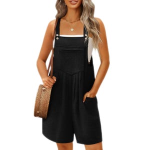 Black sleeveless romper with adjustable straps and front buttons, featuring a square neckline, a large front pocket, and loose shorts. Worn over a white top, accessorized with a woven round bag and gold jewelry.
