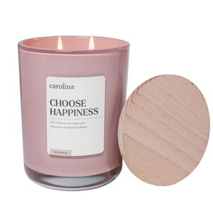 A pink candle labeled \“carolina CHOOSE HAPPINESS\“ with scents of rose water and coconut, featuring a wooden lid.