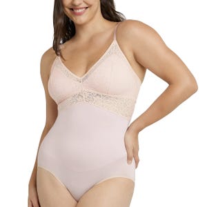 A woman is wearing a light pink lace-trimmed bodysuit with thin straps and seamless design, highlighting its lingerie style.