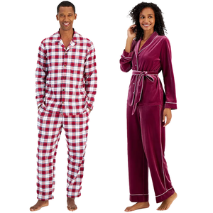 A man in a red and white checked pajama set and a woman in a burgundy velvet pajama set with white trim.