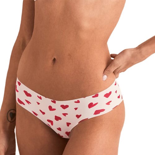 A person is wearing heart-patterned underwear and holding their hip. The person has a small heart tattoo on their wrist.